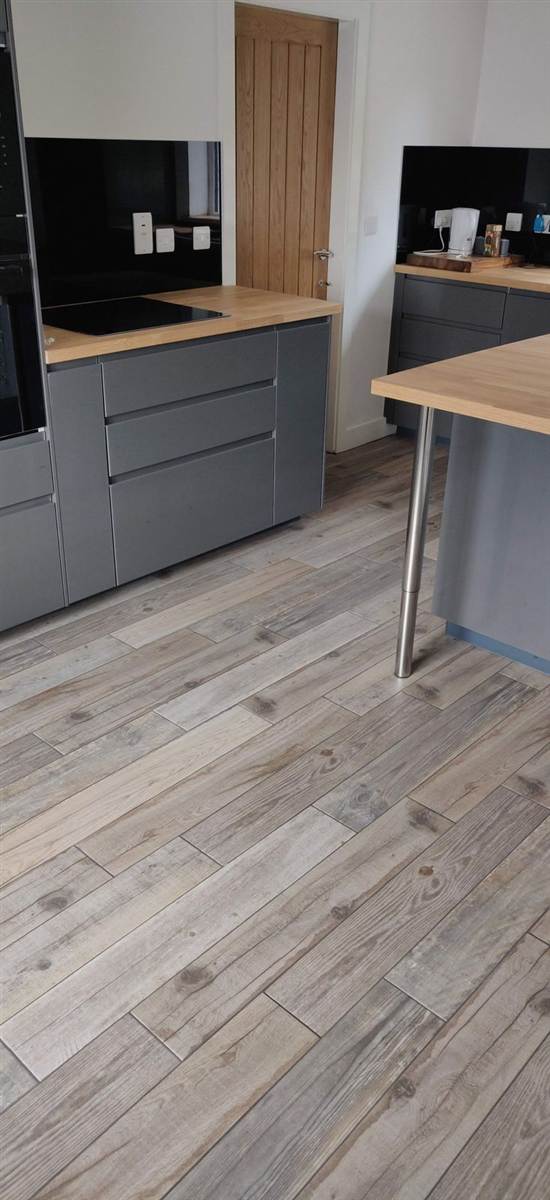 After — finished kitchen with grey handleless units, solid oak worktops, black glass splashback and wood-effect tiled floor